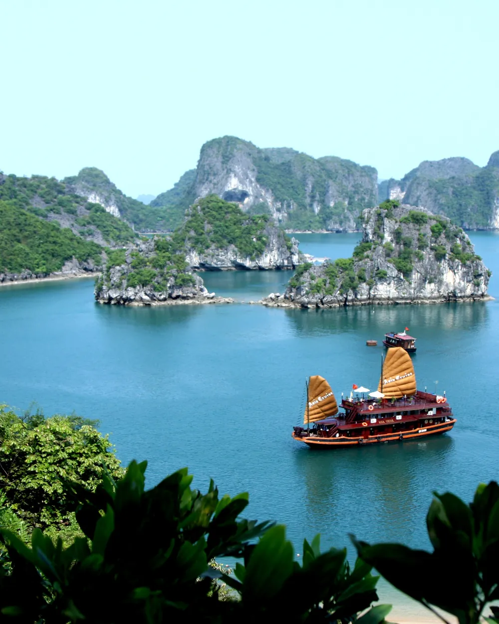 Une jonque aux voiles orangées vue d'en haut, entre les îlots de la baie d'Halong