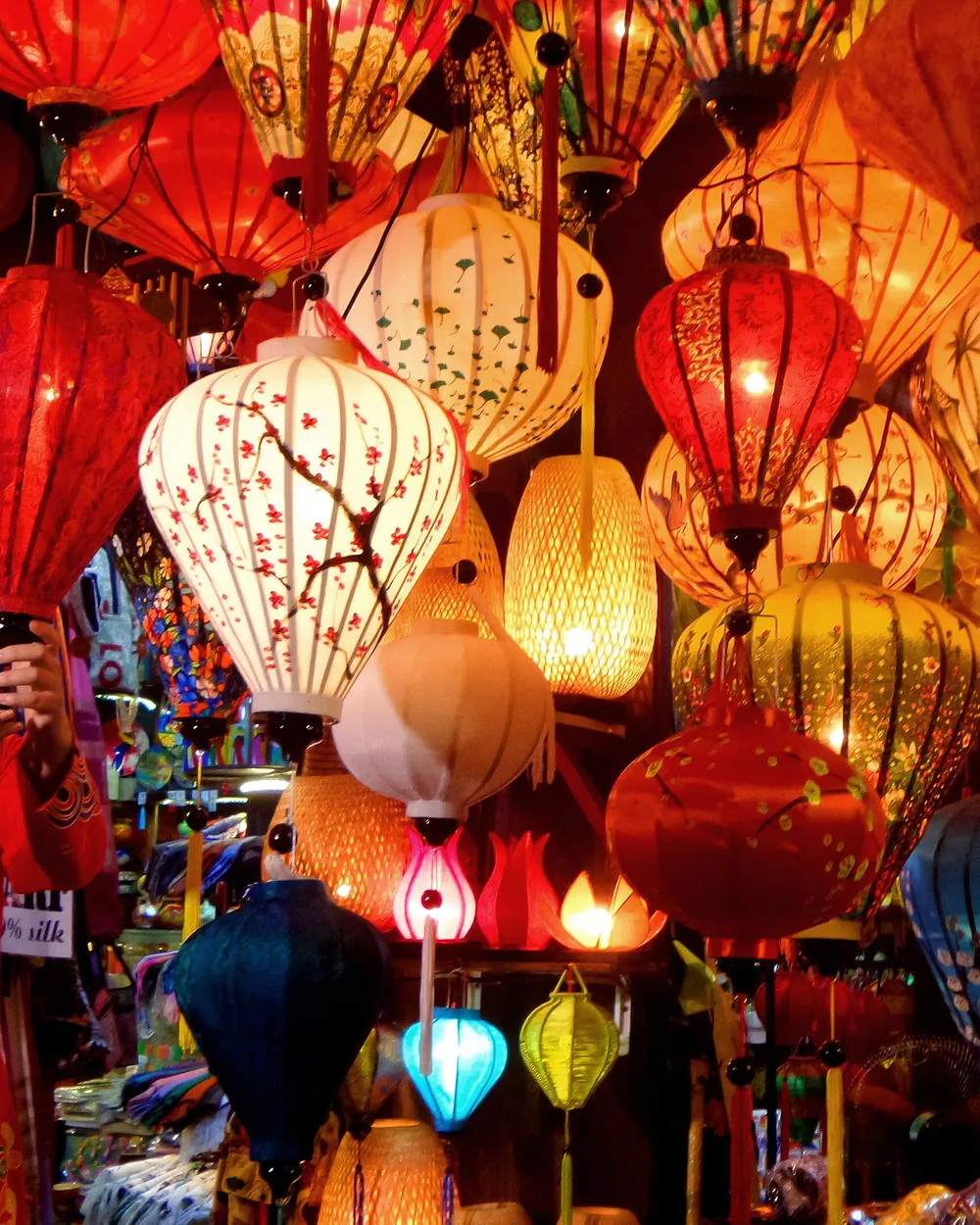 Des lanternes de soie allumées, rouges, blanches et bleues, sur un étal de Hoi An