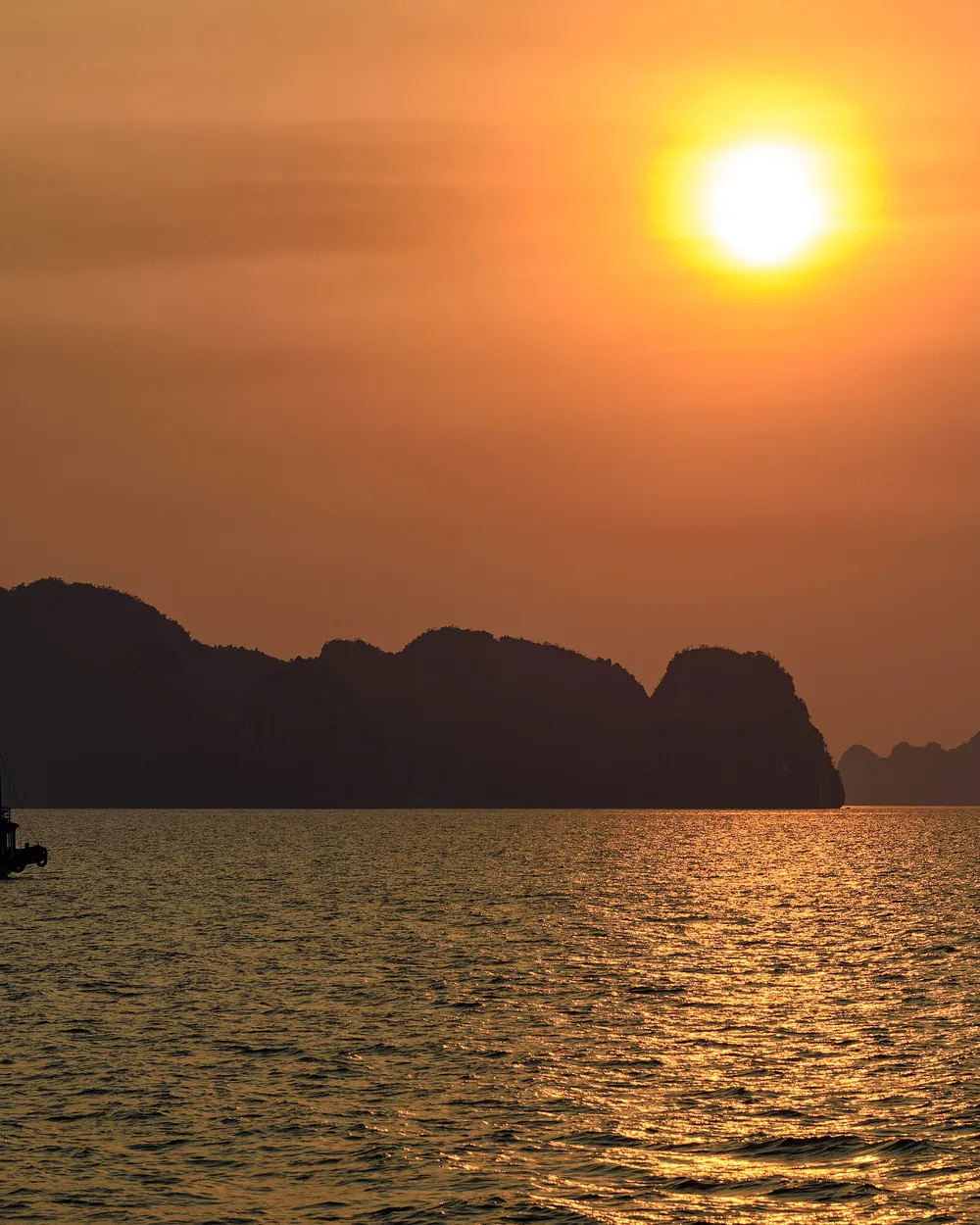 Le soleil couchant au-dessus des îlots de la baie d'Halong, sur une mer orangée